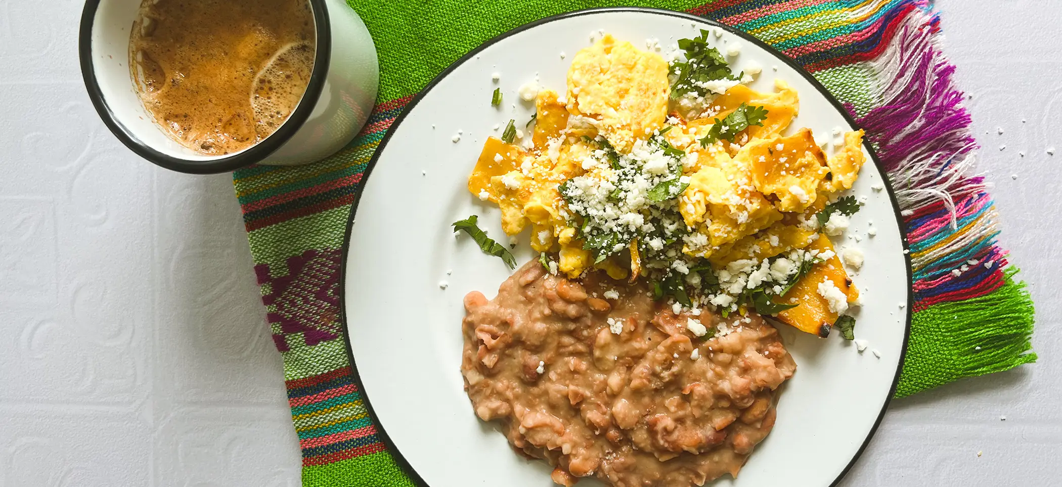 Platillo de desayuno de frijoles fritos y huevos revueltos con una taza de café